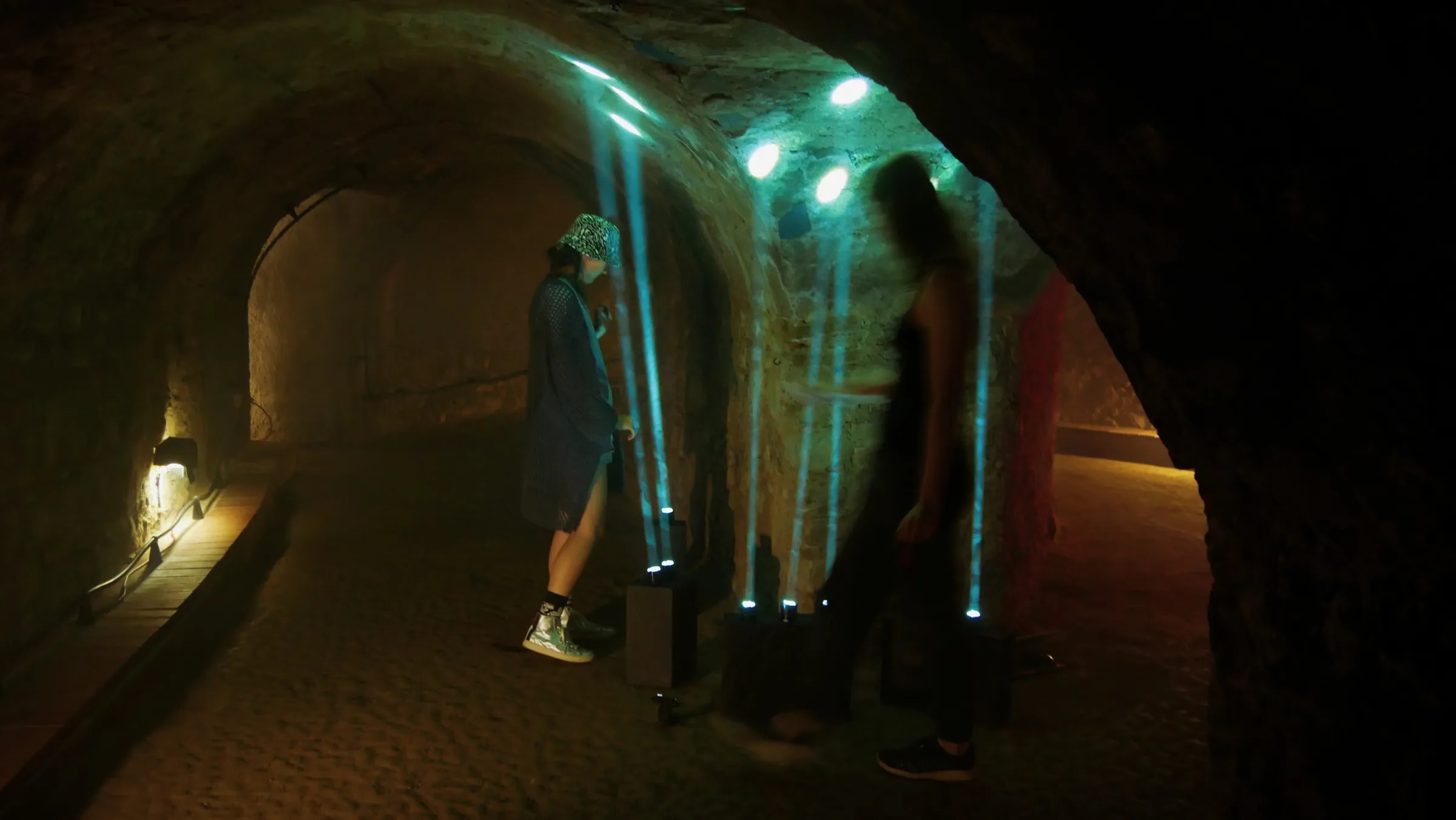 Zwei Besucherinnen spielen mit den grün-türkisen Lichtstrahlen im Gewölbe des Kellerlabyrinths Oppenheim