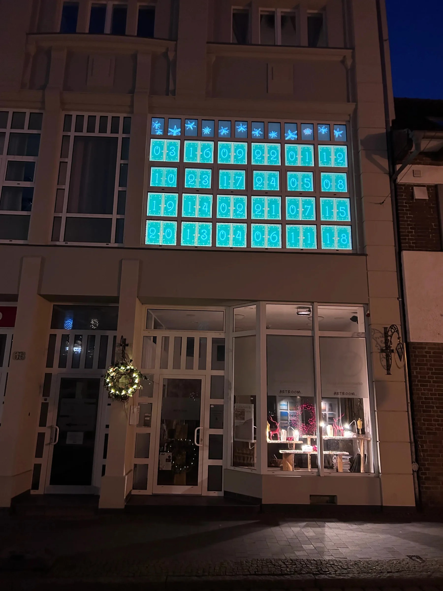 The historic department store in Barth at dusk, with the projected advent calendar of 24 turquoise doors glowing across the first-floor windows.
