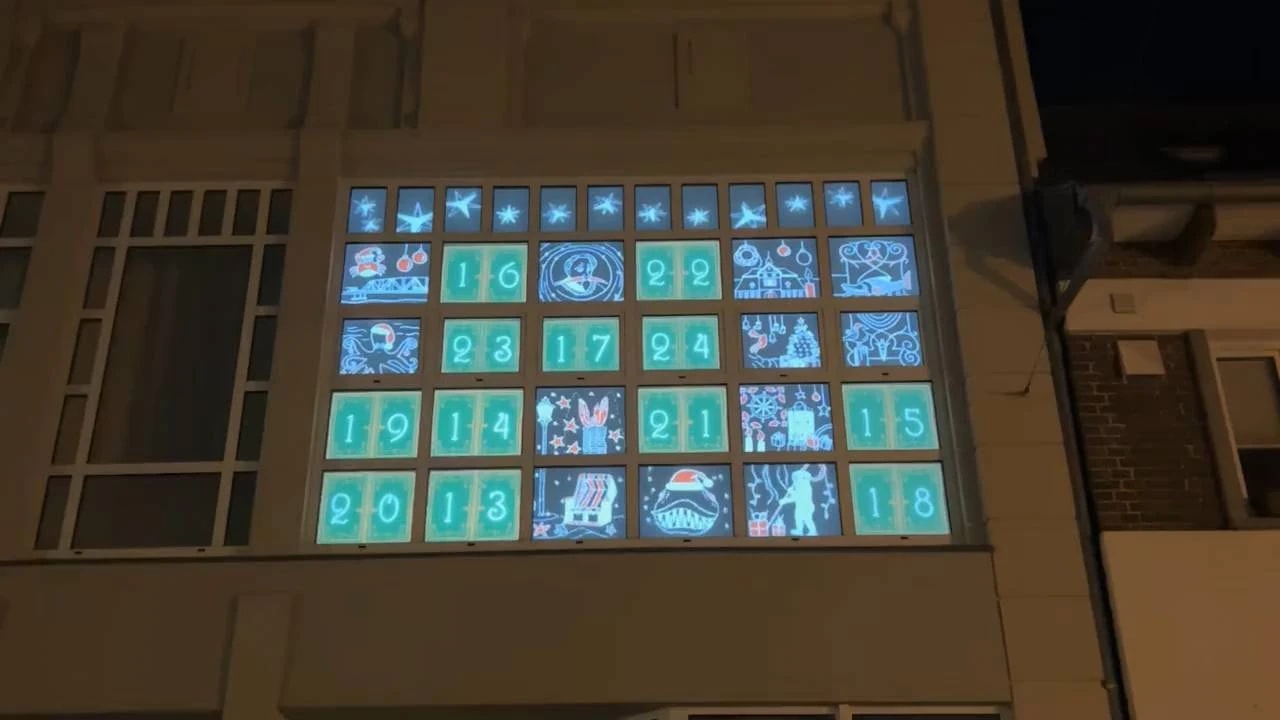 Advent calendar projection on the 24 windows of the Adventshaus Barth at night: opened doors reveal glowing winter motifs between green numbered panels.