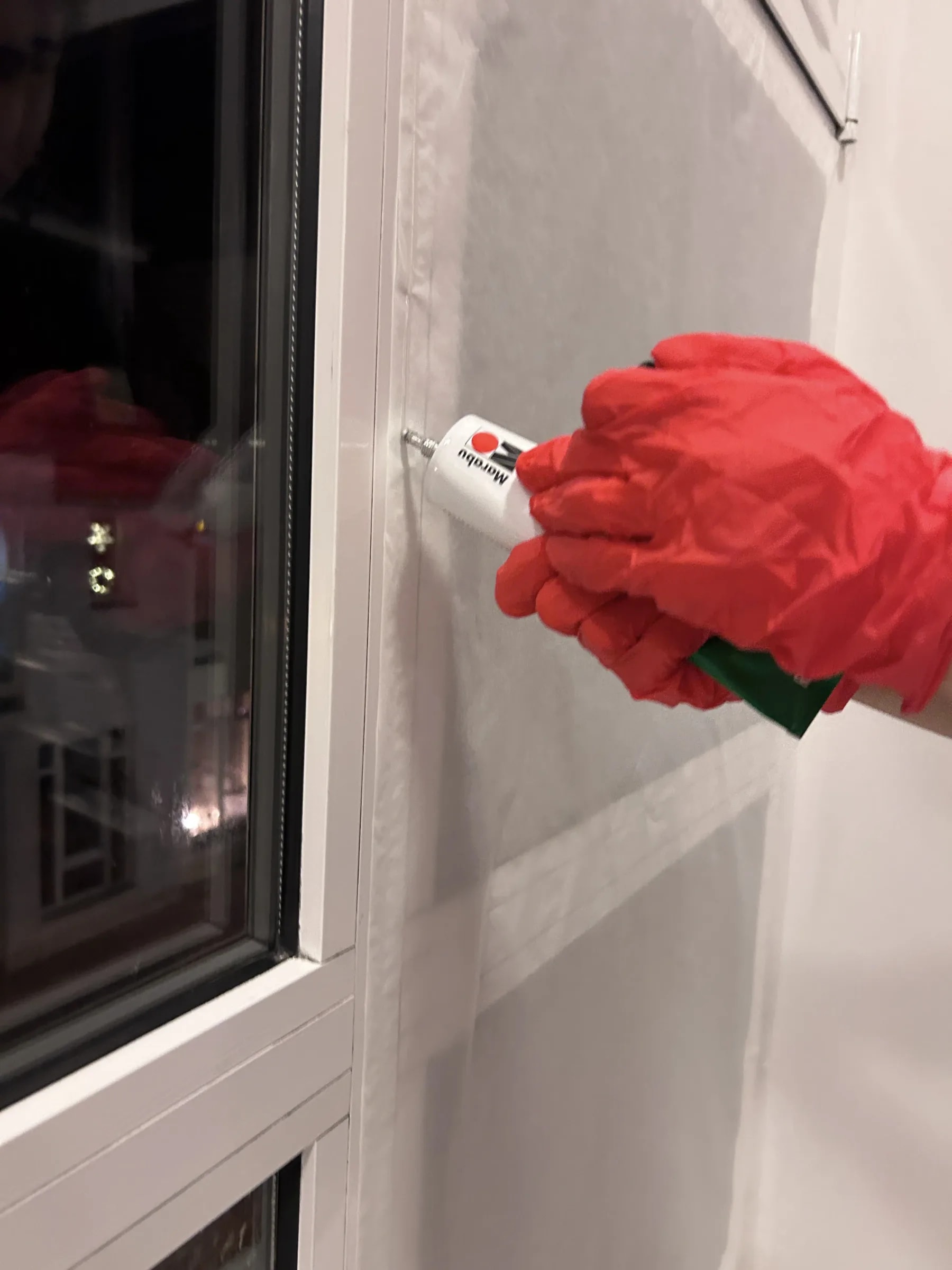 Hand in red gloves fixing projection paper to the window frame with a tube while setting up the rear projection from inside.