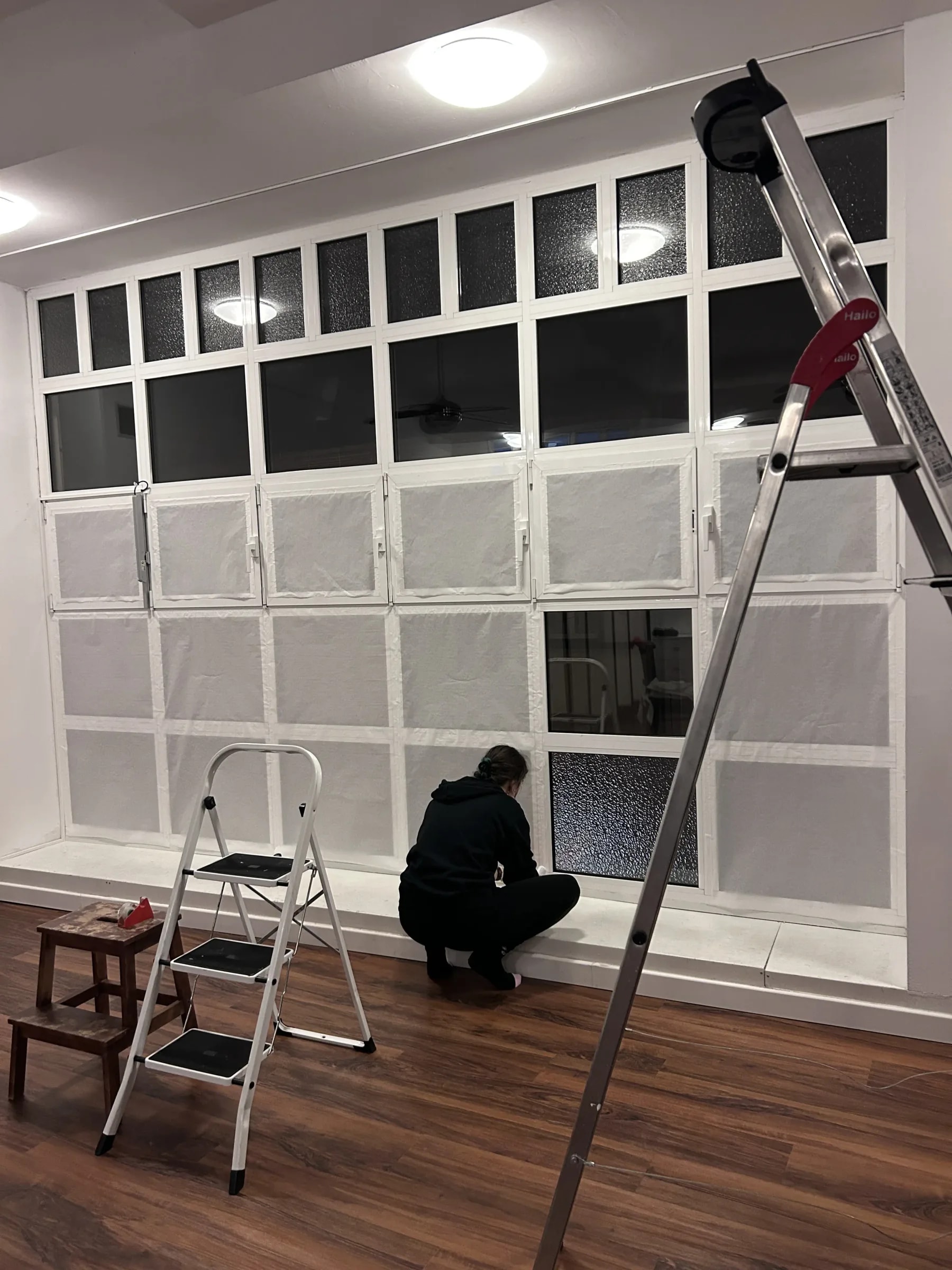 Interior behind the large window front: a person taping projection paper onto the individual panes, ladders in the foreground.